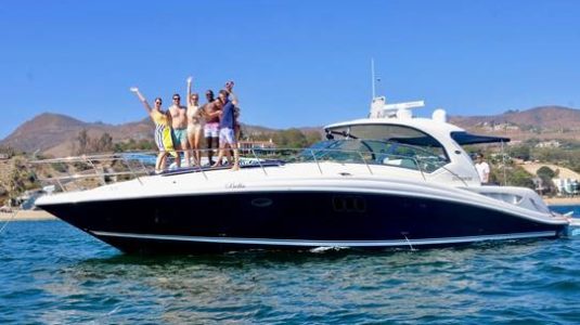 Friends standing on bow of power boat in the ocean with mountains in background