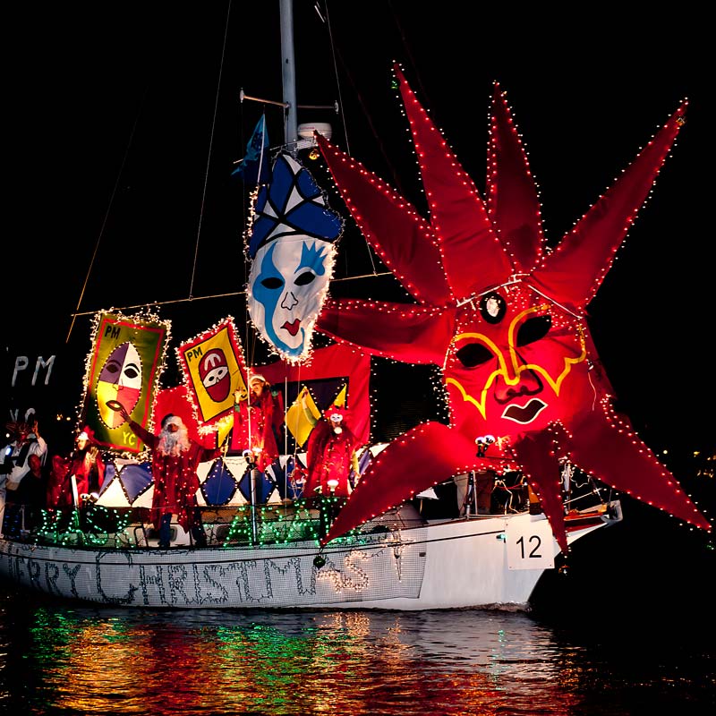 Santa Claus waving from boat decorated with lights, banners