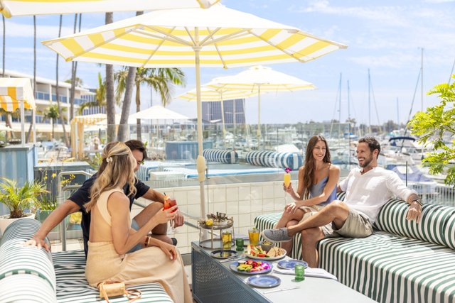 Group enjoying drinks and food at restaurant patio with yellow umbrellas next to boats in harbor